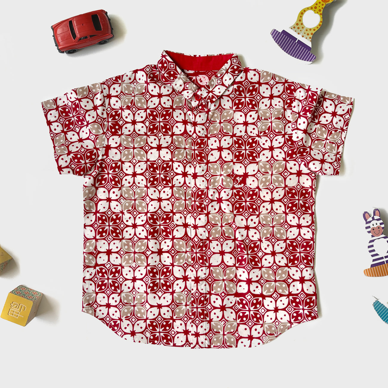 Flat lay of a red, white and beige kawung batik shirt for boys