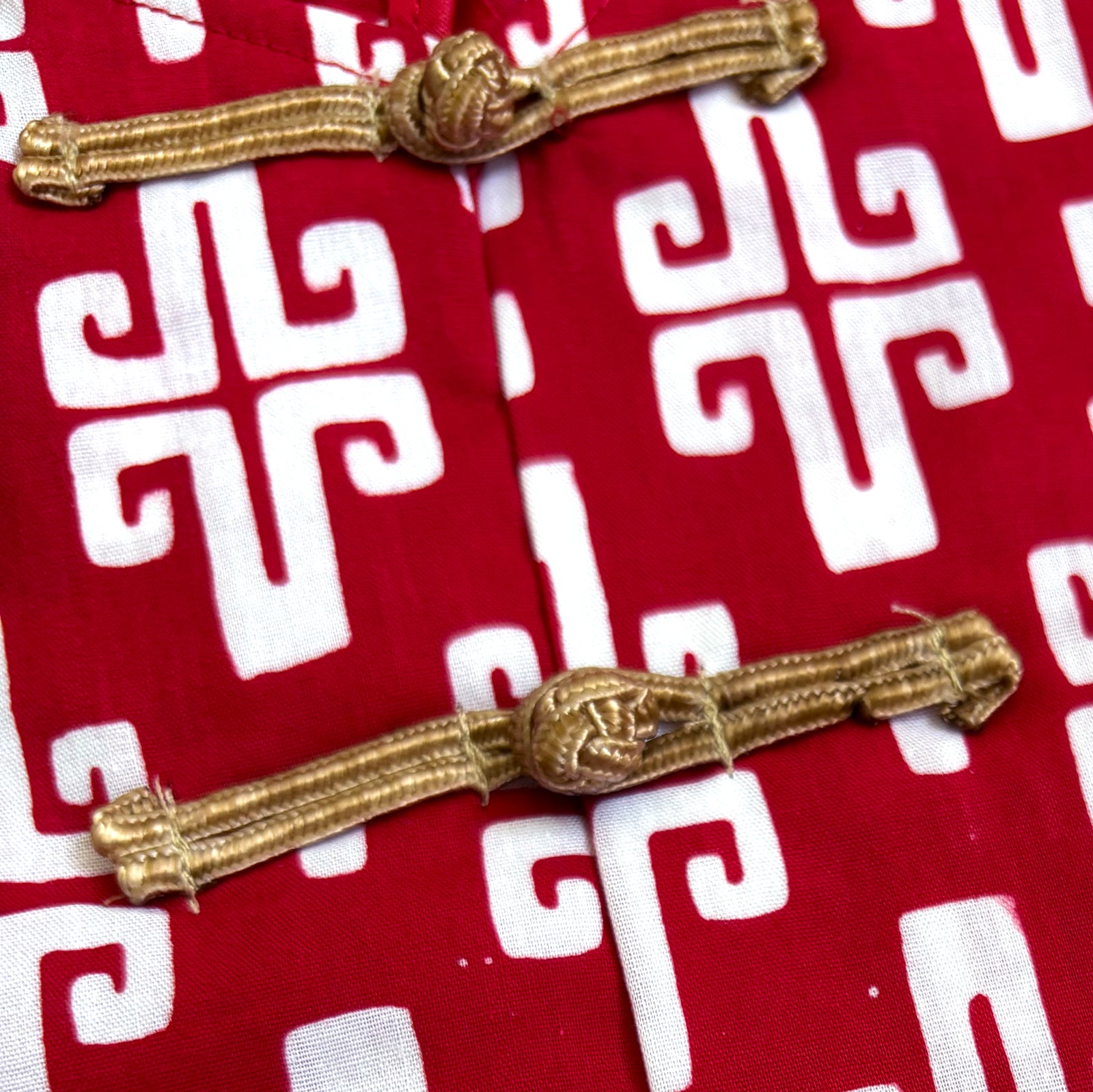 Close up of gold frog buttons and the hand-stamped ikat motif on a red shirt