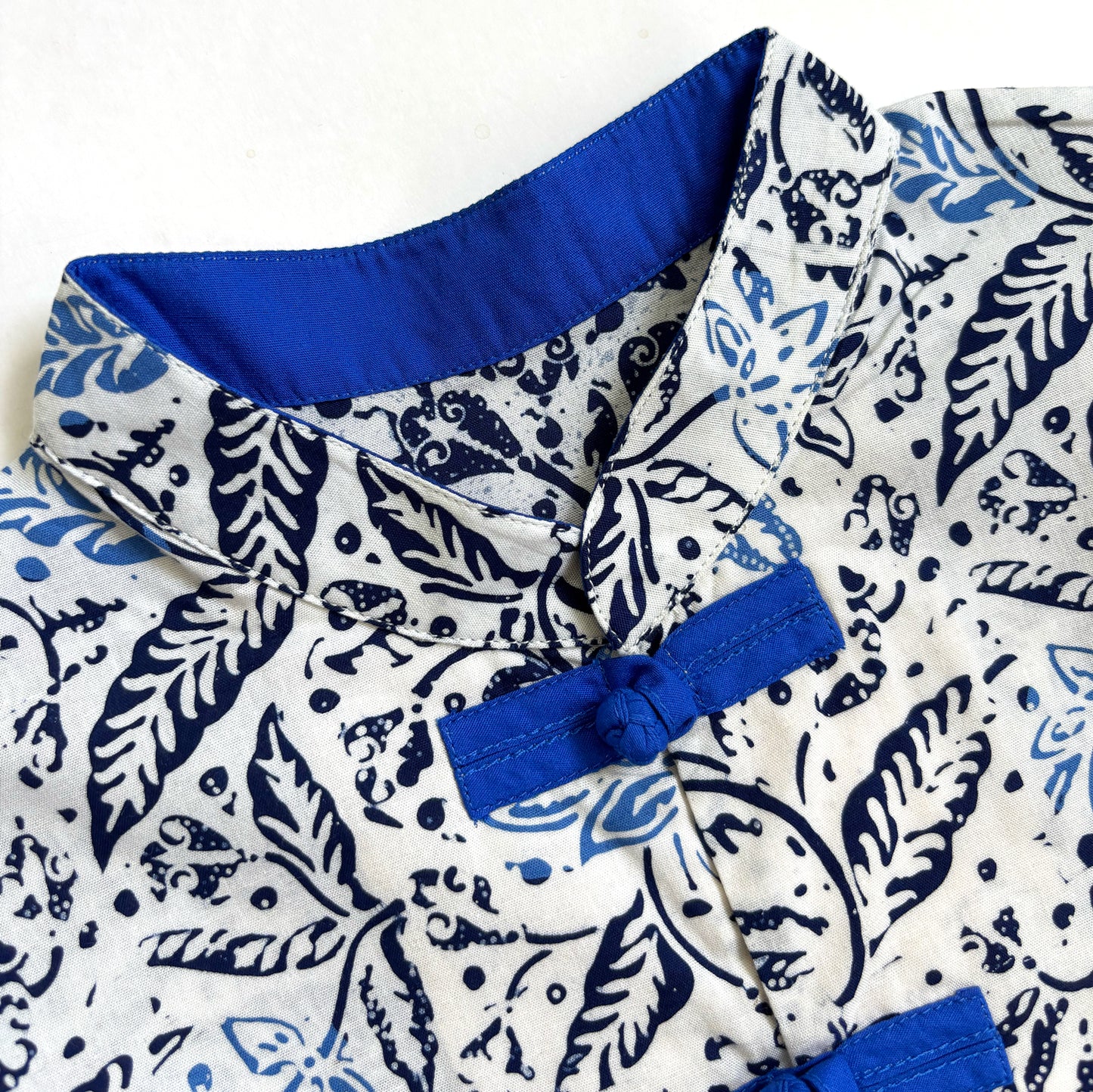 Close up of a blue mandarin collar lining and frog buttons on a blue and white floral batik shirt