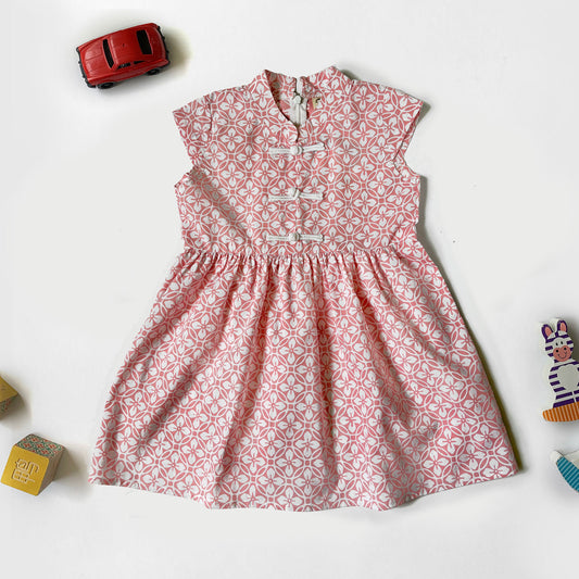 Flat lay of a pink and white kawung batik cheongsam dress with a mandarin collar and frog buttons