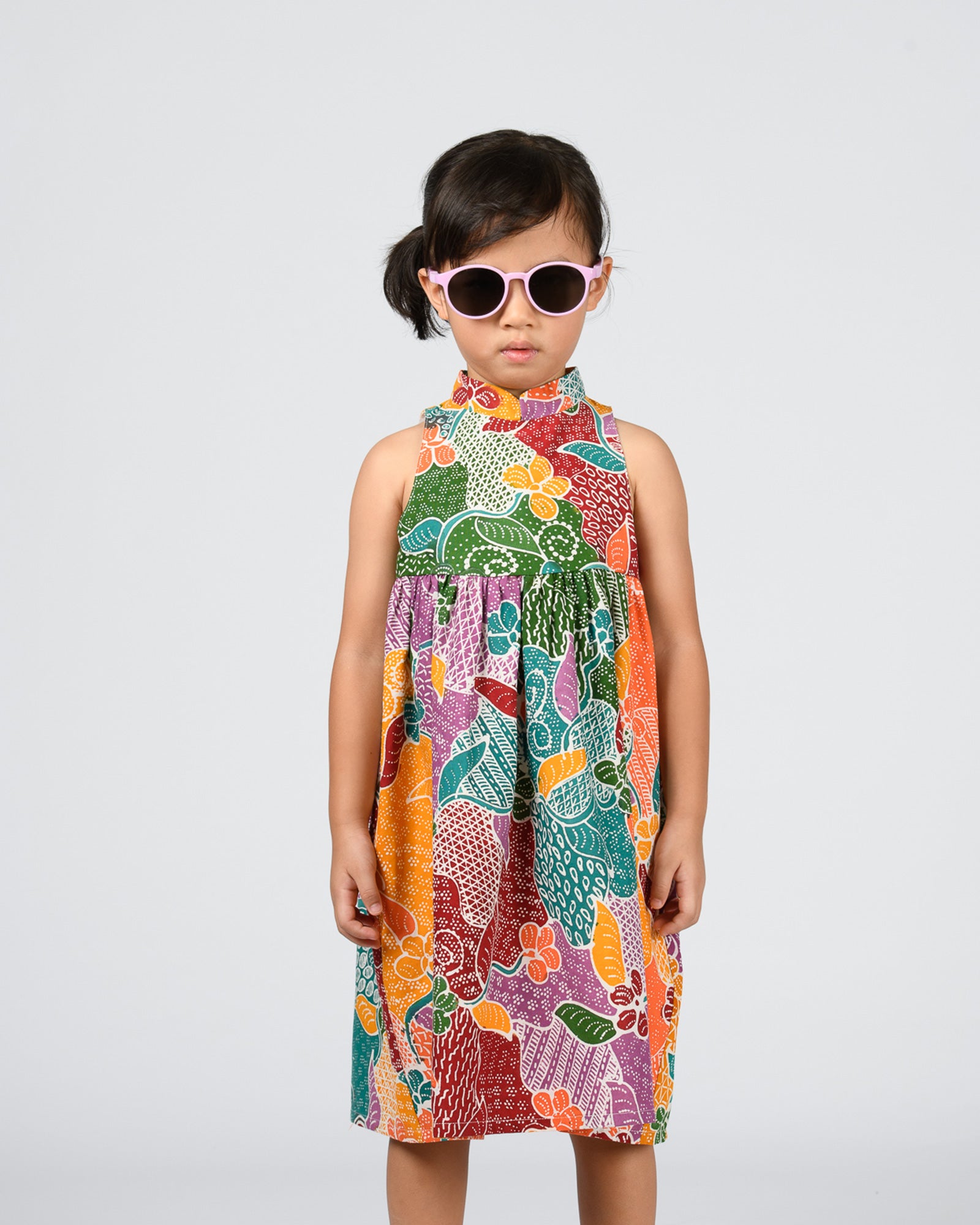 Child wearing a colorful batik patterned dress on a white background