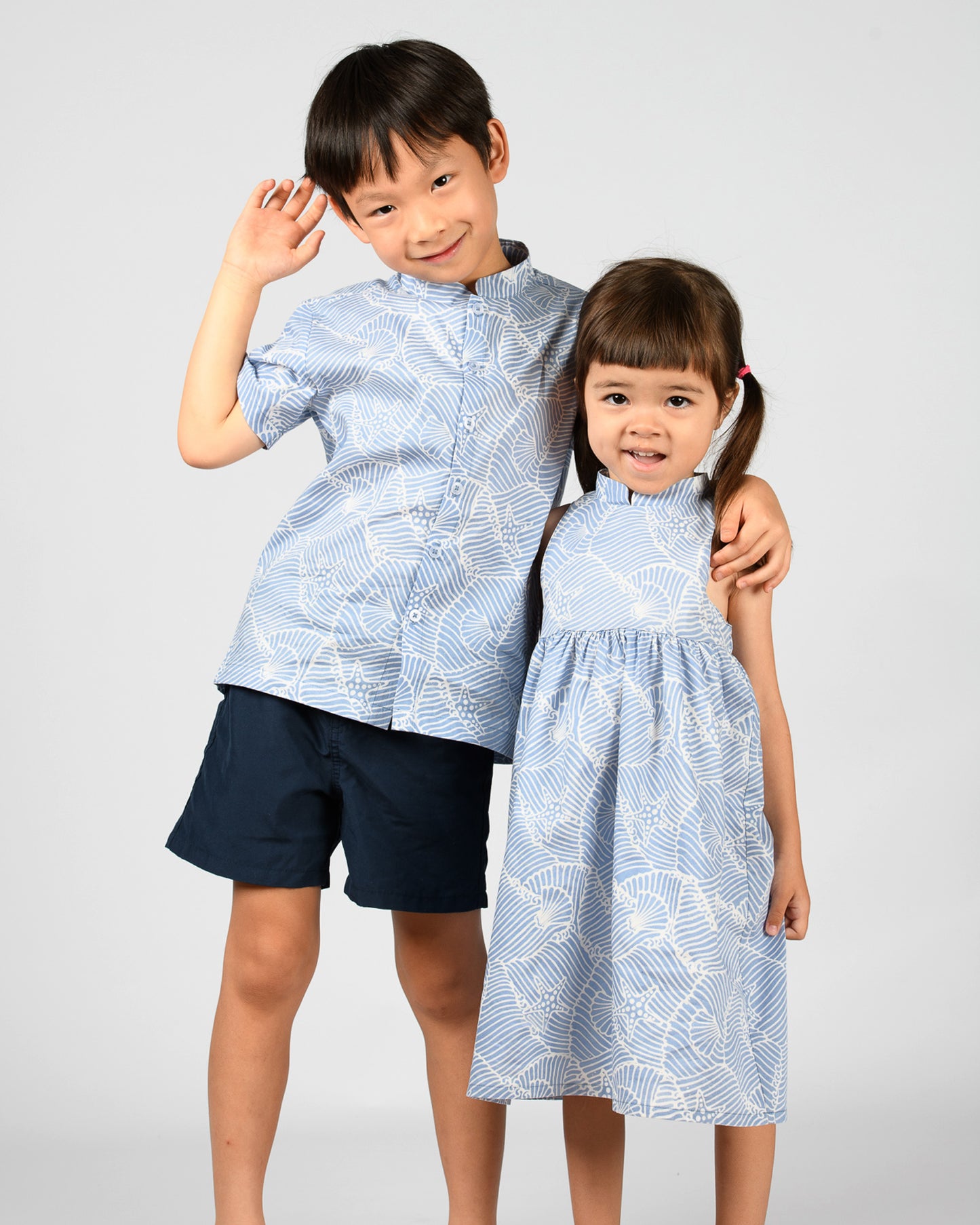 Two children wearing matching blue and white batik outfits on a plain background