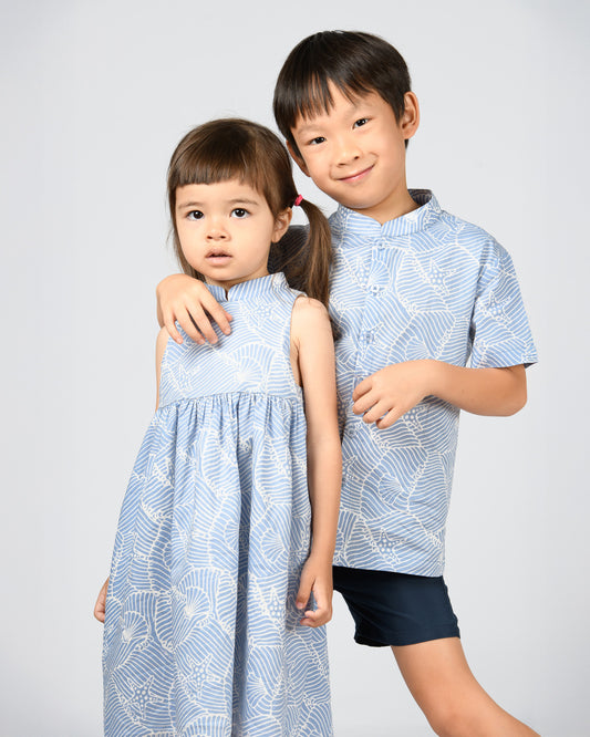 Two children wearing matching blue and white batik outfits on a plain background