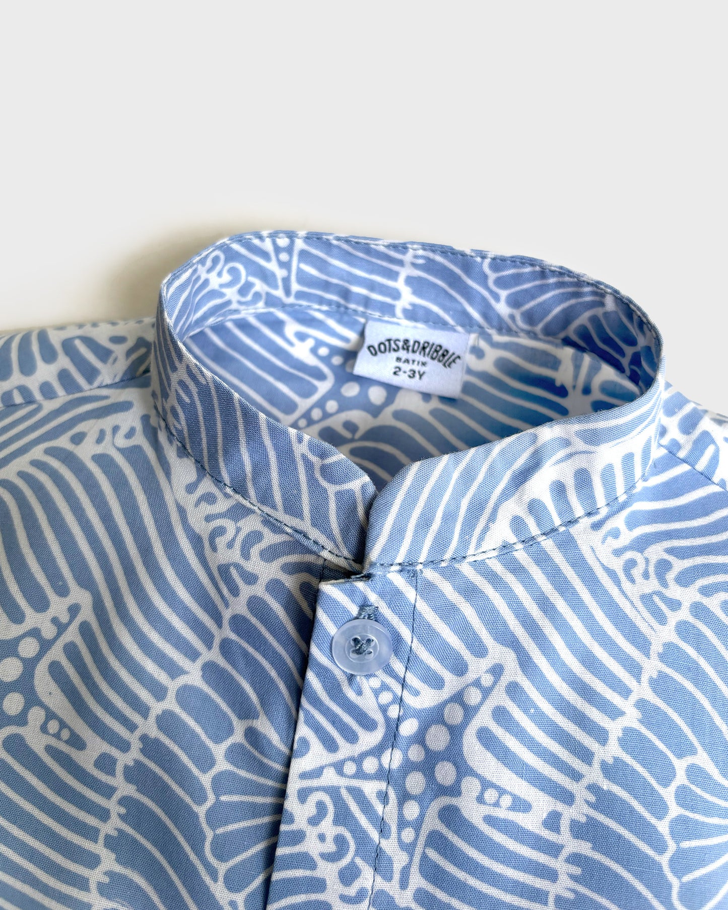 Close-up of a blue and white batik seashell patterned shirt with a brand label on a light background