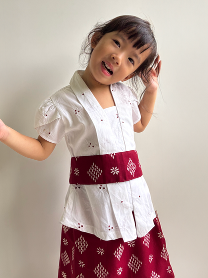 Girl wearing a white kartini kebaya top with a sparkle patterned belt and a red batik skirt