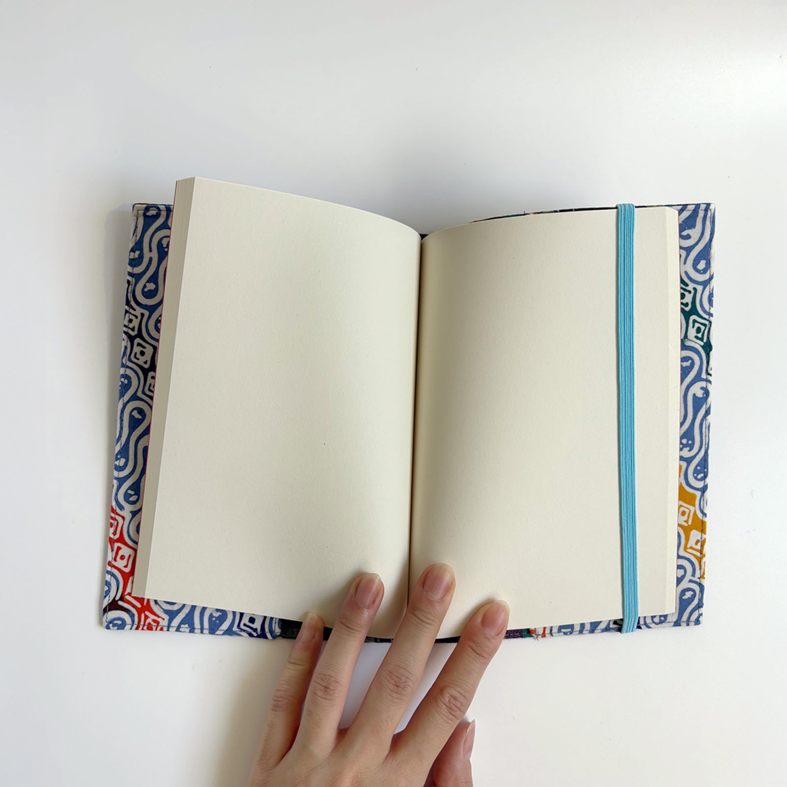 Open notebook with decorative binding held by a hand on a white background
