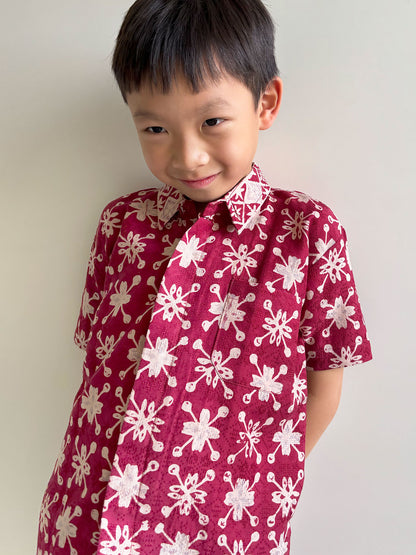 Child wearing a red and gold batik shirt against a plain background