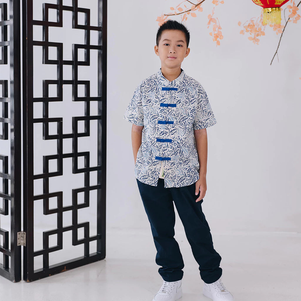 Child wearing a batik white shirt with blue accents standing in front of a decorative screen.
