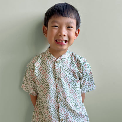 Smiling boy wearing a light pink and green handstamped batik shirt on dobby cotton for Hari Raya
