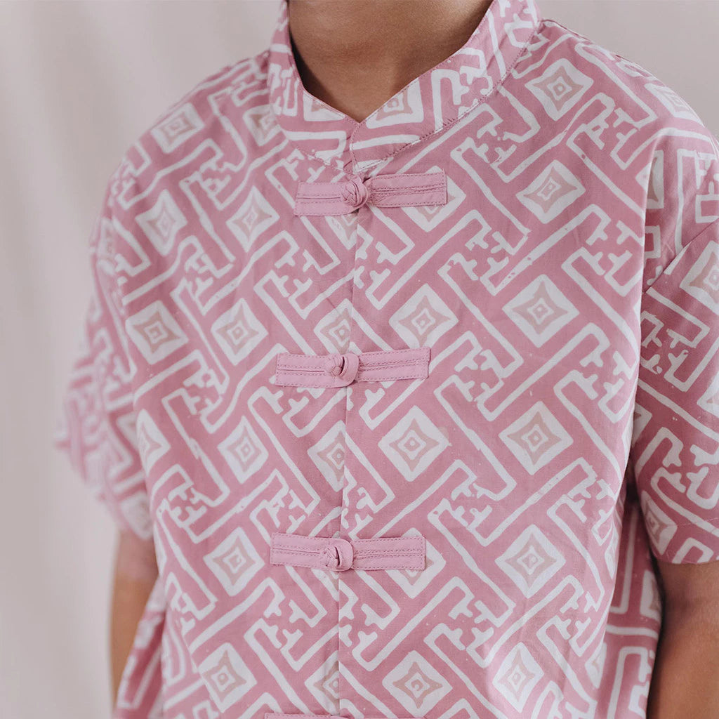 Person wearing a pink and white batik cheongsam with frog buttons on a plain background