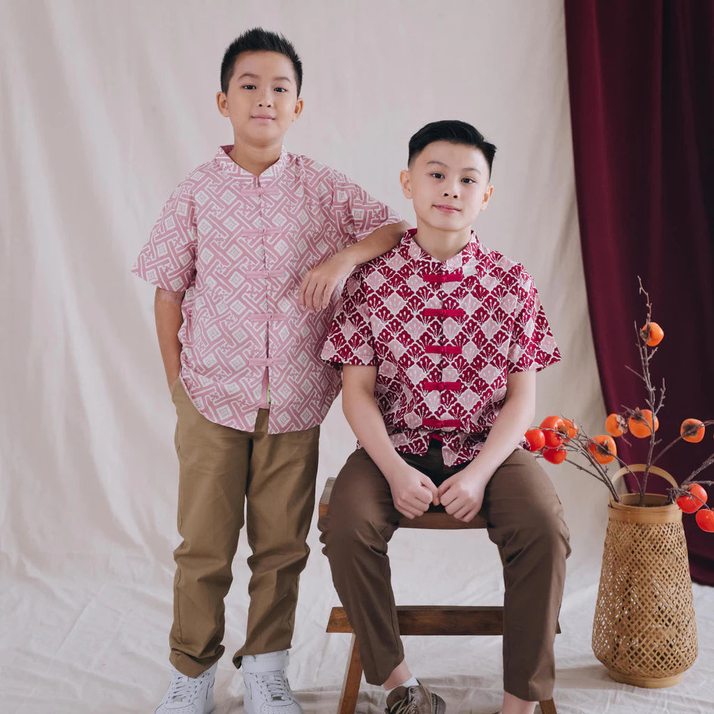 Two boys in complimentary Chinese New Year batik cheongsams posing in front of a plain background with a decorative vase.